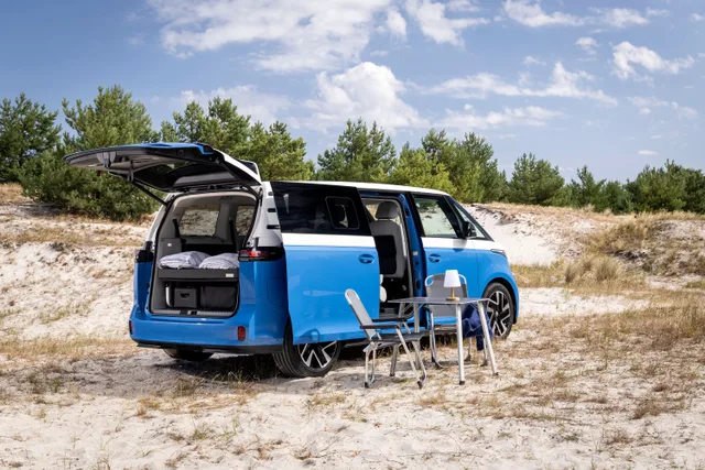 Volkswagen ID. California Cruise i blå og hvid holder i klitterne med åbne døre og opstillet campingbord